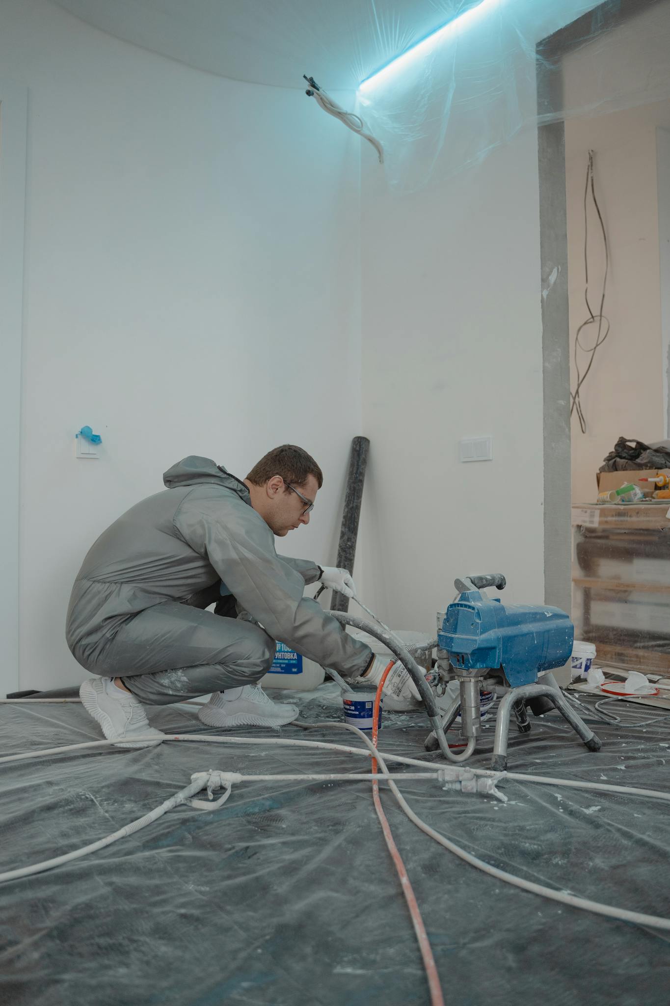 Worker using machinery in a renovation setting, wearing protective gear indoors.
